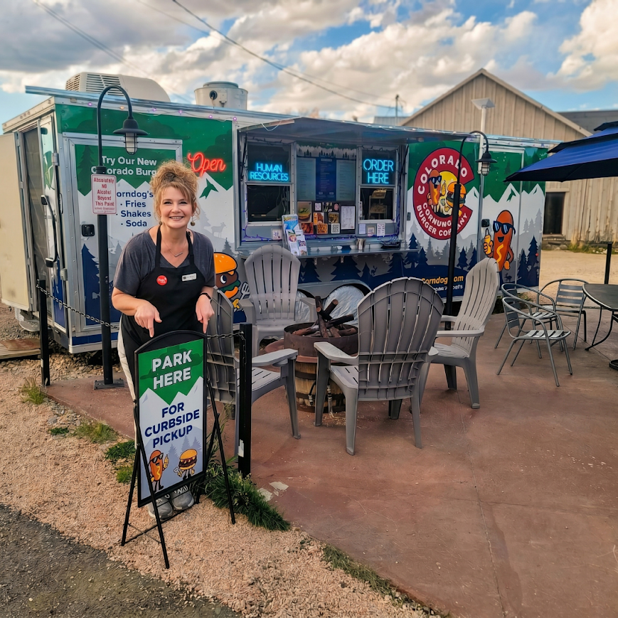 Curbside pickup area at Colorado Corndog & Burger Company in Fraser, Colorado with owner pointing to the designated parking sign